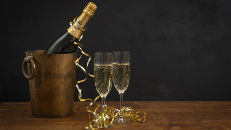 A champagne bottle in a tin bucket with two flutes of champagne