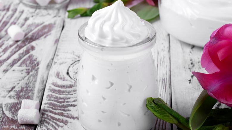 A jar ofmarshmallow creme on a wooden table dusted with sugar