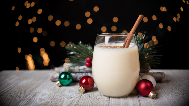 A glass of eggnog on a wooden table surrounded by holiday decorations