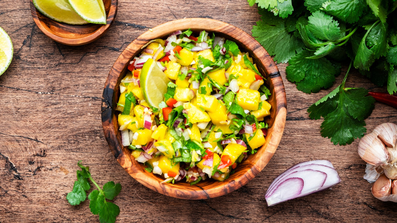 Wooden bowl of mango salsa with limes, cilantro, and garlic