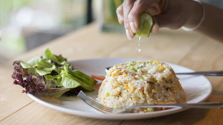 hand squeezing lime into plate of fried rice for enhanced, fresh flavors