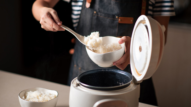 woman with apron scooping fresh cooked jasmine rice from pot into two small white ceramic bowls