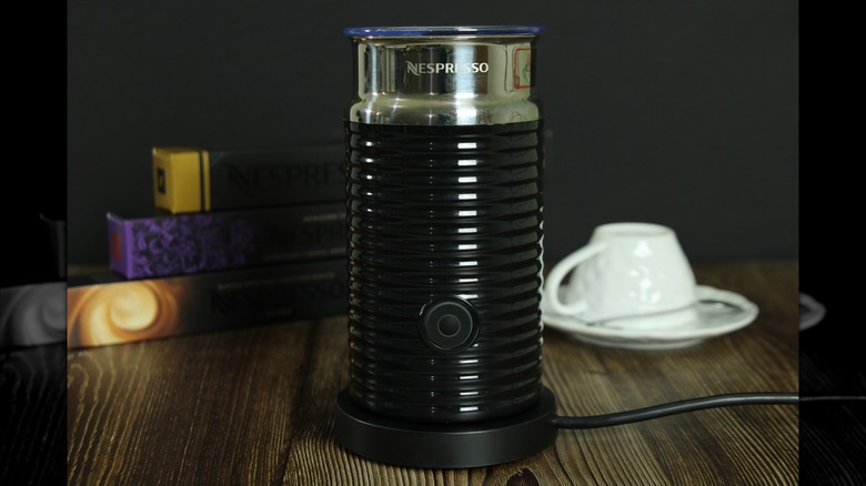 A Nespresso milk frother in front of books and a white tea cup