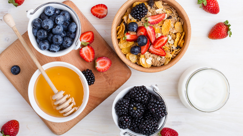 A bowl of cereal with berries and small containers of honey, berries, and milk