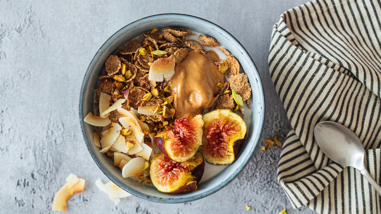 A bowl of cereal with figs, coconut chips, and peanut butter