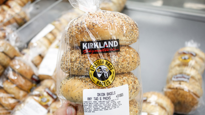 A hand holds a bag of Kirkland onion bagels