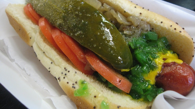 A Chicago-style hot dog, with a pickle spear, tomato slices, onion and, of course, mustard, on a poppy seed bun.