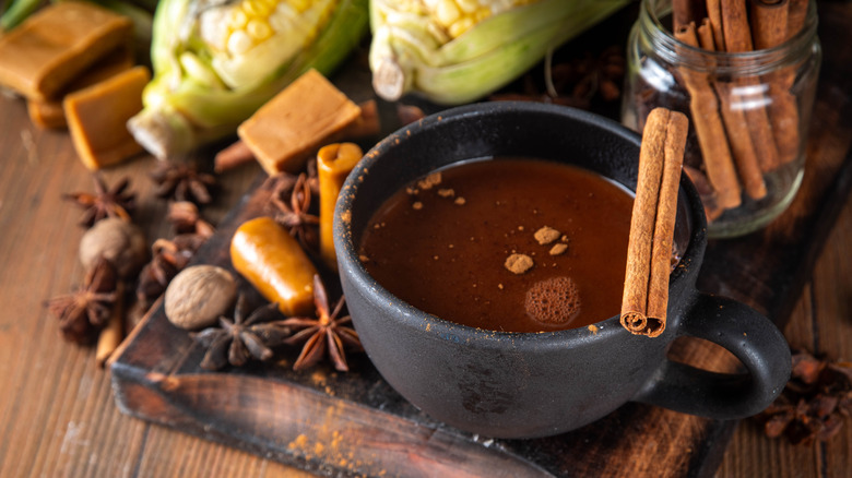 Black mug with chocolate, next to spices and corn