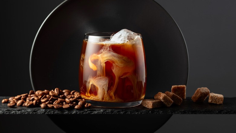 A glass of iced coffee with cream on a black background with coffee beans.