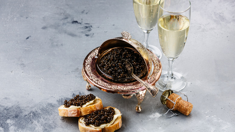 Two champagne flutes, a bowl of caviar, and two slices of bread with caviar