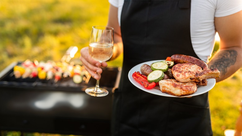 man holding plate of steak and glass of white wine