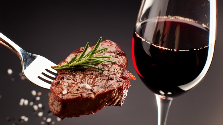 cut of meat on fork next to red wine in a glass