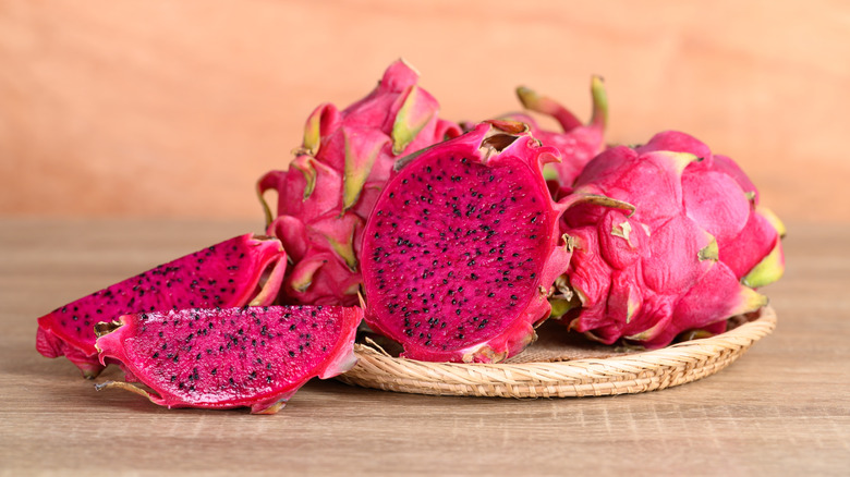 Red dragon fruit on a flat wooden basket with one sliced in half