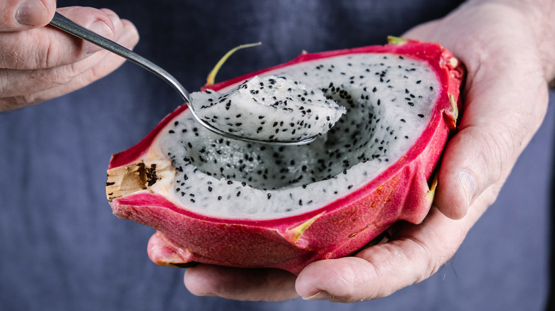 A set of hands holding and scooping half of a dragon fruit