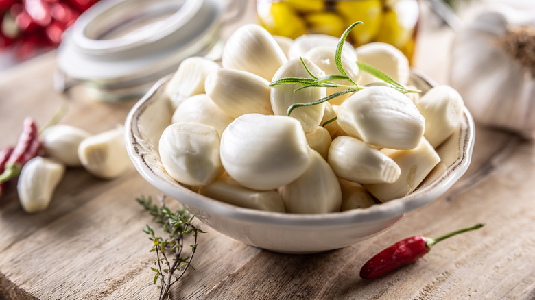 peeled garlic in a white bowl decorated with some sort of green herb garnish