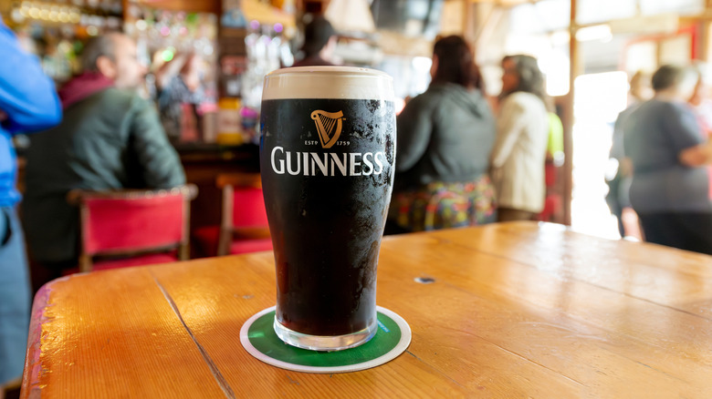 A pint of Guinness with appropriate foamy head on a wooden table in a busy bar