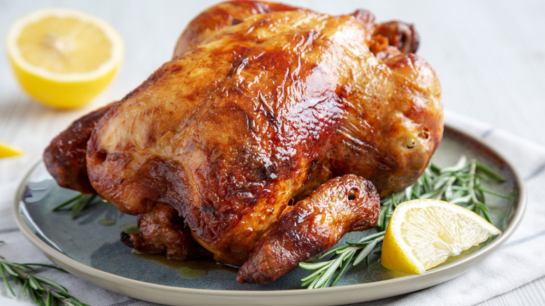 whole roast chicken on a plate with rosemary and lemon slices