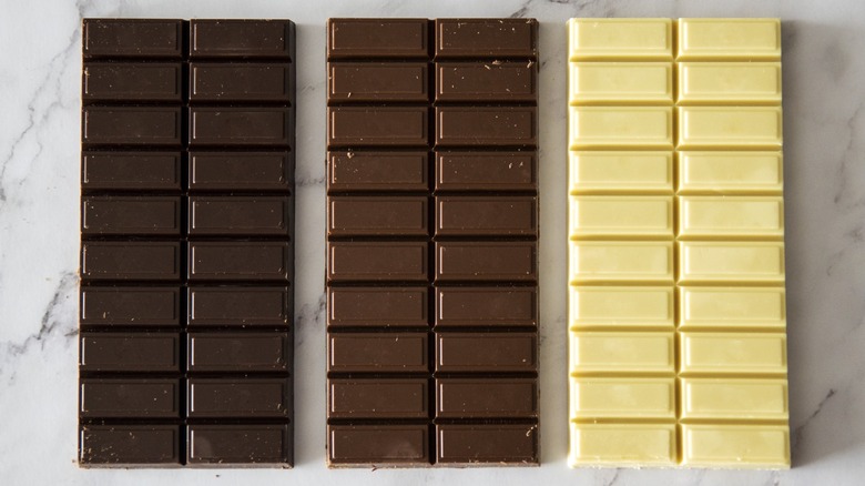 Dark, milk, and white blocks of chocolate sitting on a counter.