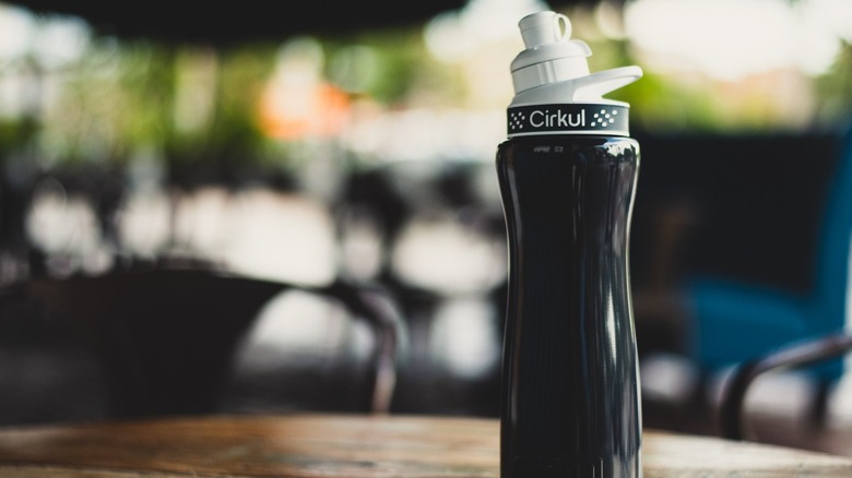 A black Cirkul water bottle on a wooden table at an outdoor restaurant