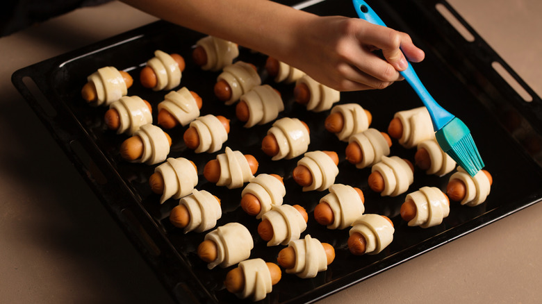 Brushing uncooked pigs in a blanket on baking sheet