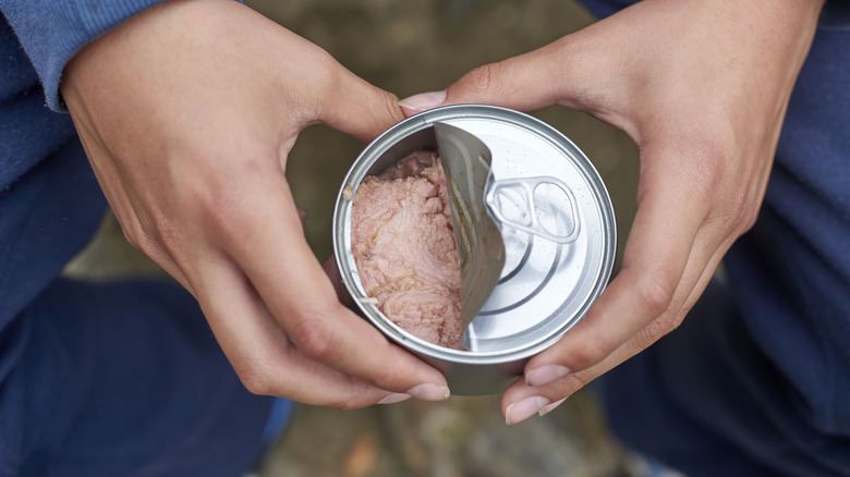 hands holding a partially opened can of tuna