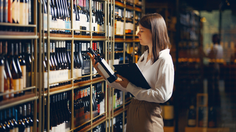 A woman looking at a wine bottle.