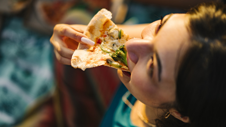 woman eating a slice of pizza with broccoli on it