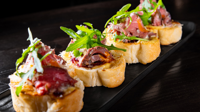 Black plate with crostini with beef and arugula on top