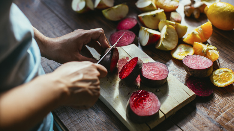 woman chopping beets on a cutting board with stains