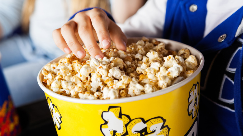 Person eating from a bucket of movie theater popcorn