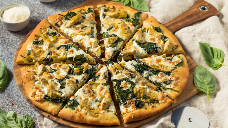 A sliced spinach artichoke pizza on a wooden pizza board