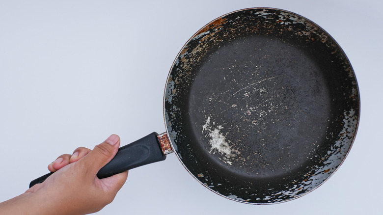 a hand holding out a nonstick skillet that is scraped and scratched