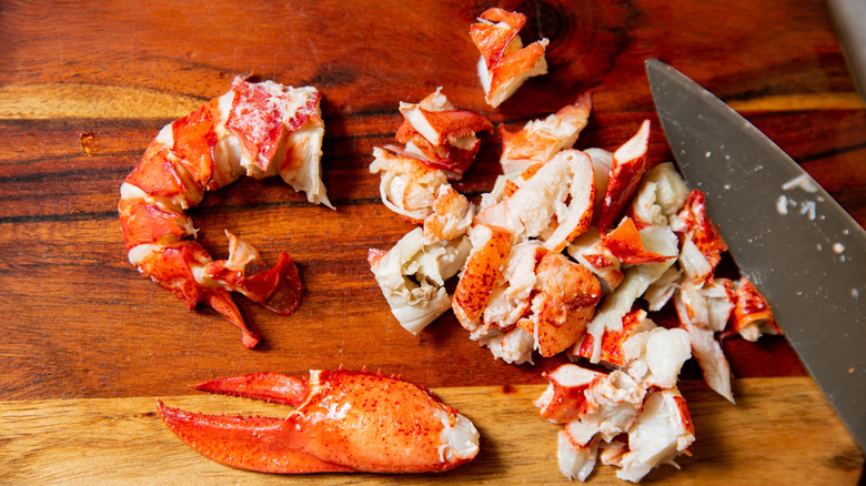 Chunks of cooked lobster meat on board with large knife