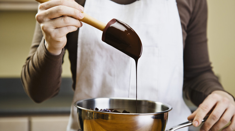 melting chocolate on a double boiler holding spatula dripping chocolate