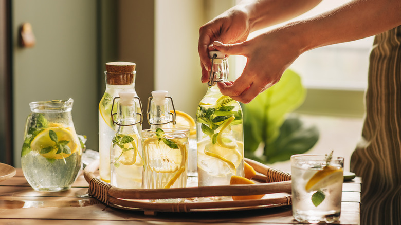 person sealing fresh mixture of lemonade in several glass bottles on table inside