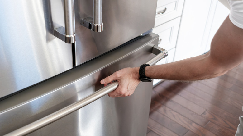 A person reaching to open a stainless steel freezer