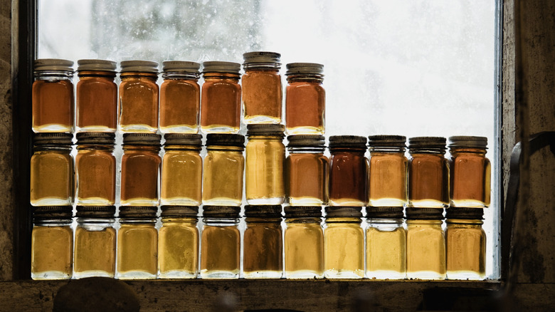 a variety of jarred maple syrups of different colors in a window