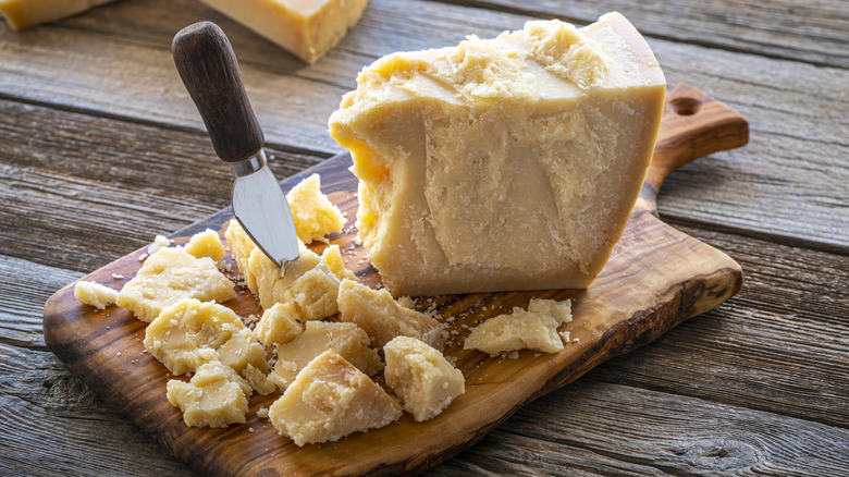 Block and crumbles of Parmigiano Reggiano cheese on wooden cutting board