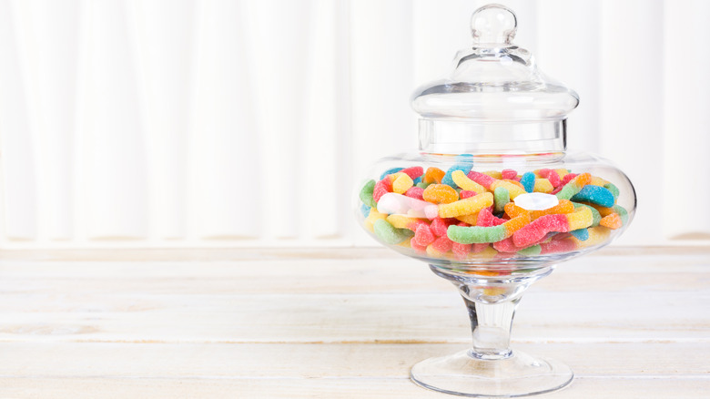 Gummy worms in a glass candy jar sitting on a white surface