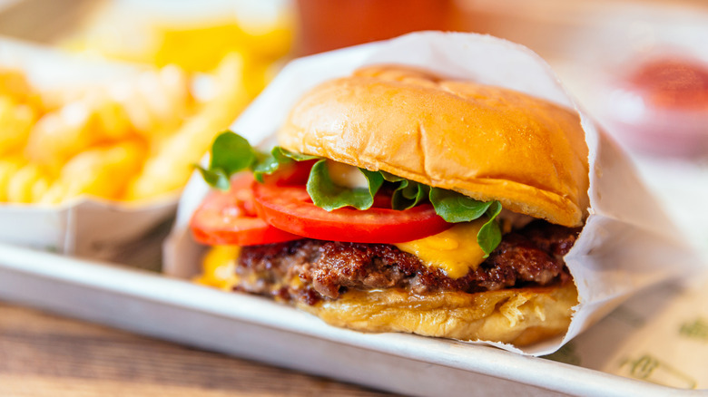 A hamburger in a paper sleeve and blurred fries in the background