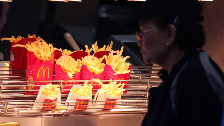 McDonald's fries sitting under a heat lamp and a McDonald's employee in foreground