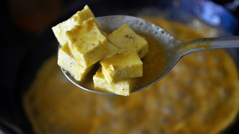 A spoonful of paneer with gravy hanging above a pot.