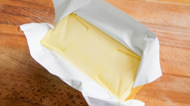 Stick of butter partially unwrapped sitting on wooden counter.