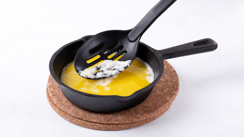 Black spoon skimming foam off melted butter in pan