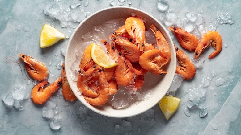 Shrimp in a bowl of ice water and lemon on the side with a marble background