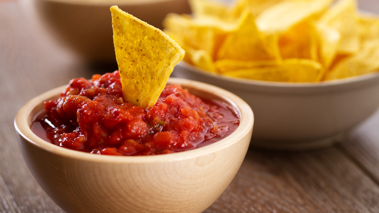 Dark ceramic bowl filled with salsa, tortilla chips are on the table next to the bowl.