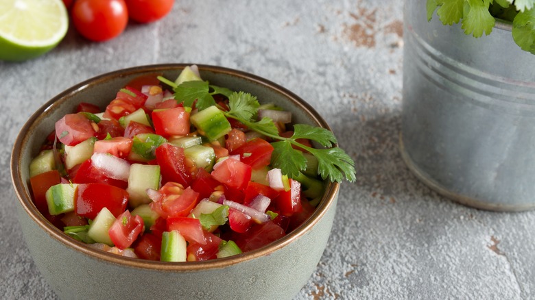 Grey ceramic bowl of salsa surrounded by ingredients