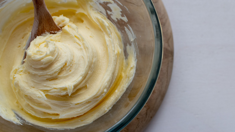 Thick vanilla buttercream in a glass bowl with wooden spoon