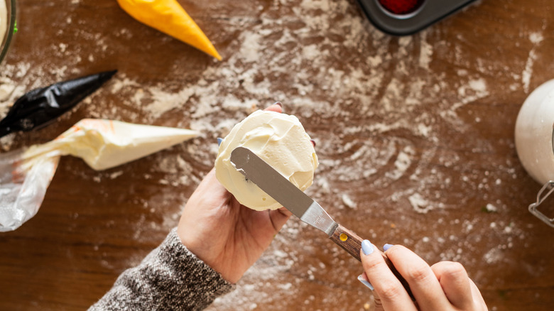 Vanilla cupcake being frosted with offset spatula