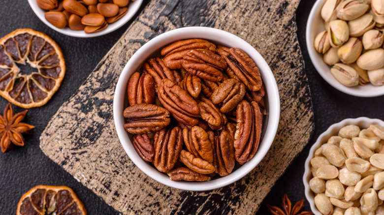 pecans in a ramekin on a rustic wood board with other nuts around